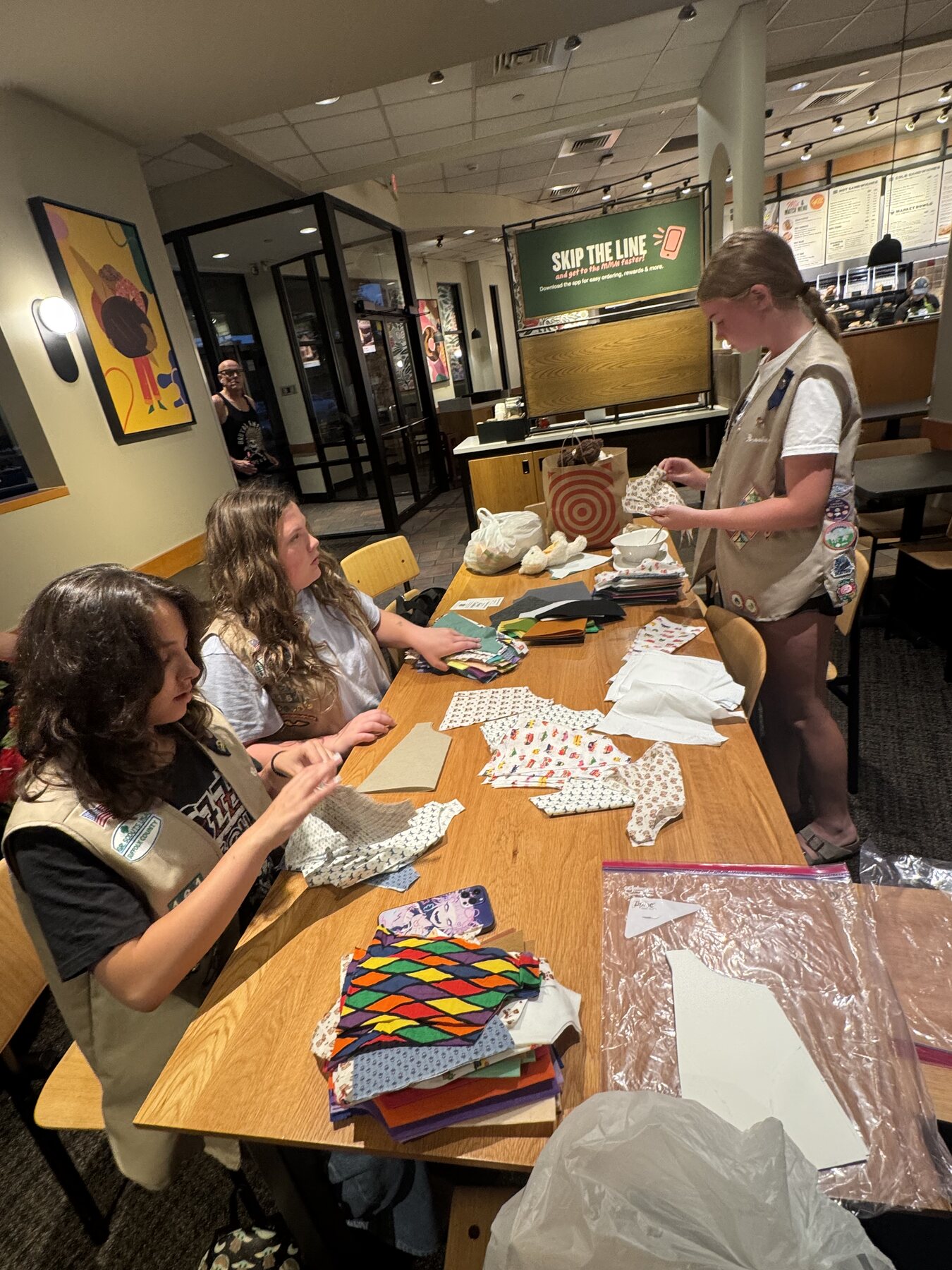 Cavan, Brooke, and Gabriella assembling capes together around a table