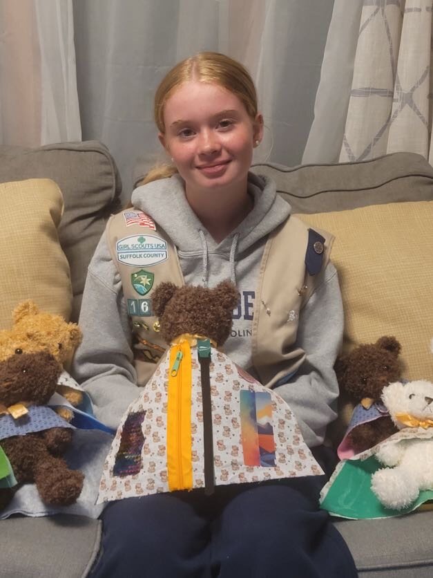 A Girl Scout holding a teddy bear wearing its completed sensory cape